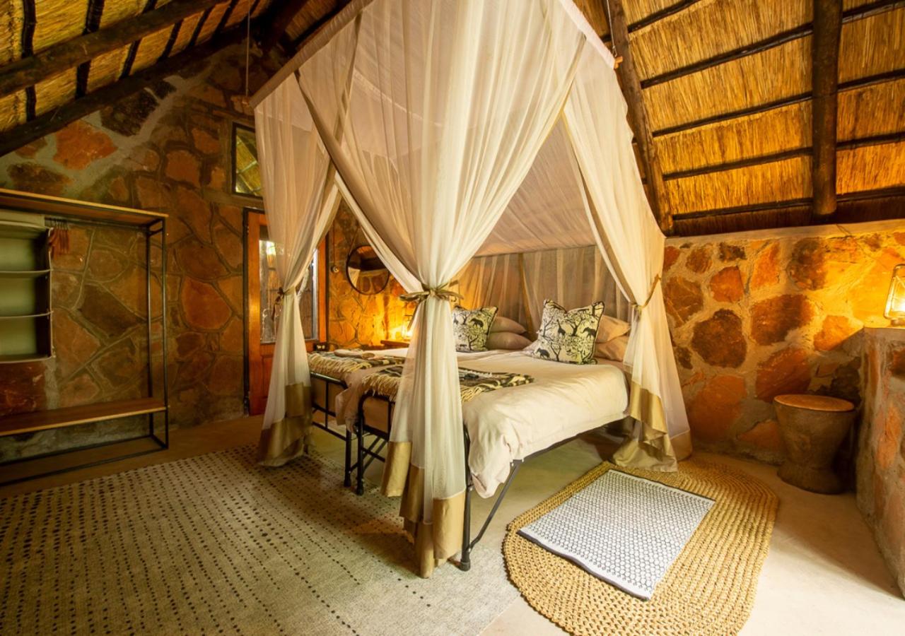 A stone-and-thatch room with a netted bed at Bumbusi Wilderness Camp
